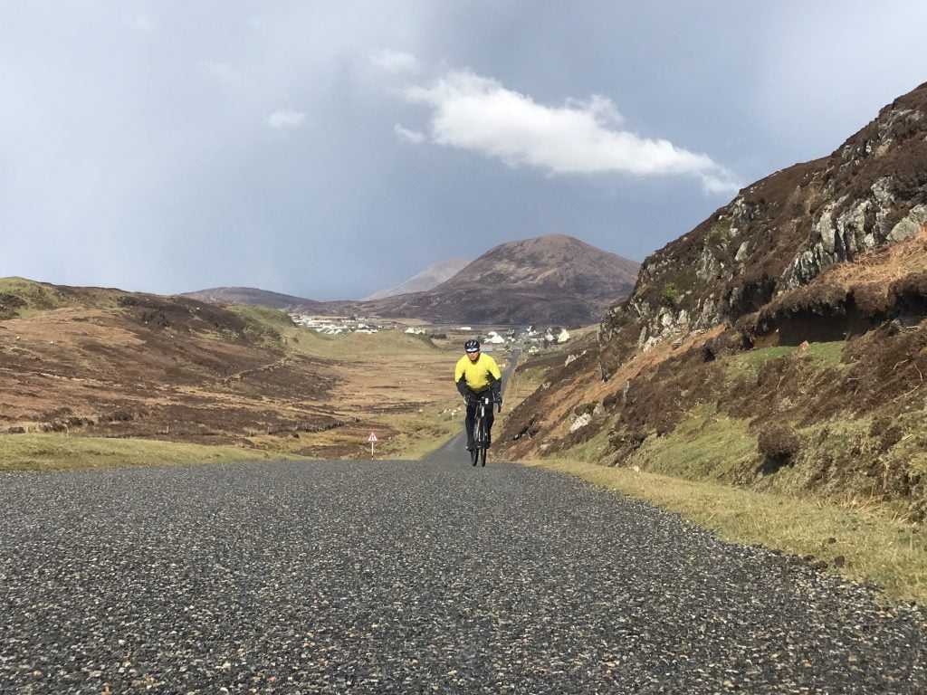 A cyclist rides along the Hebridean Way on Harris with mountains behind him NCN 780