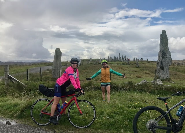 Two female cyclists cycling on the Outer Hebrides posing for a photograph at the Callanish Standing Stones