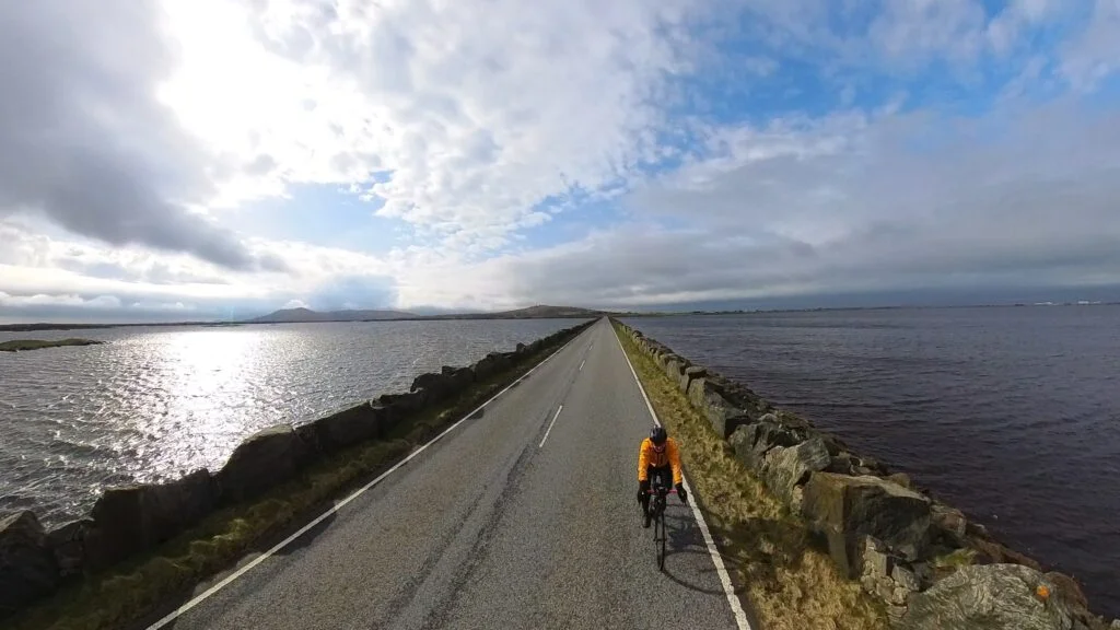 A solo cyclist on a Skinny Tyres Ltd fully supported road cycling holiday, rides across the causeway between Benbecula and North Uist on the Hebridean Way cycling route at high tide.