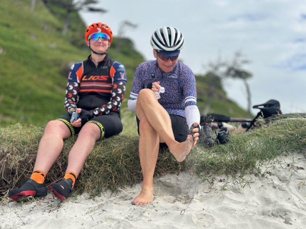 Two female cyclists on a Skinny Tyres fully supported road cycling holiday are cleaning sand off their feet after paddling in the Atlantic Ocean at Calgarry Bay on the Island of Mull in Scotland.