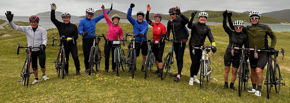 A group of cyclists line up at the start of the Hebridean Way cycling tour with Skinny Tyres. Below them is a caption that reads "What a fantastic trip and what a brilliant cycle touring company Skinny Tyres are! I've done quite a lot of tours with other companies and while the standard is always high in my experience, Skinny Tyres is the best company I've ever toured with."