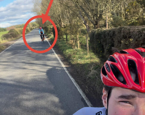 A young cyclist takes a photo of themselves with their dad struggling to keep up in the back ground.