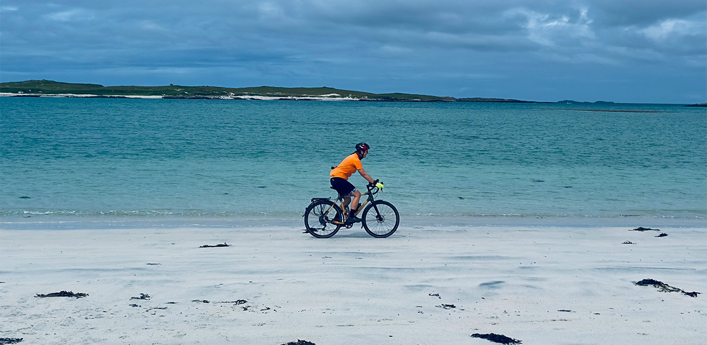 Cyclist riding along the white sands of North Uist on the Hebridean Way cycling route, Outer Hebrides with Skinny Tyres