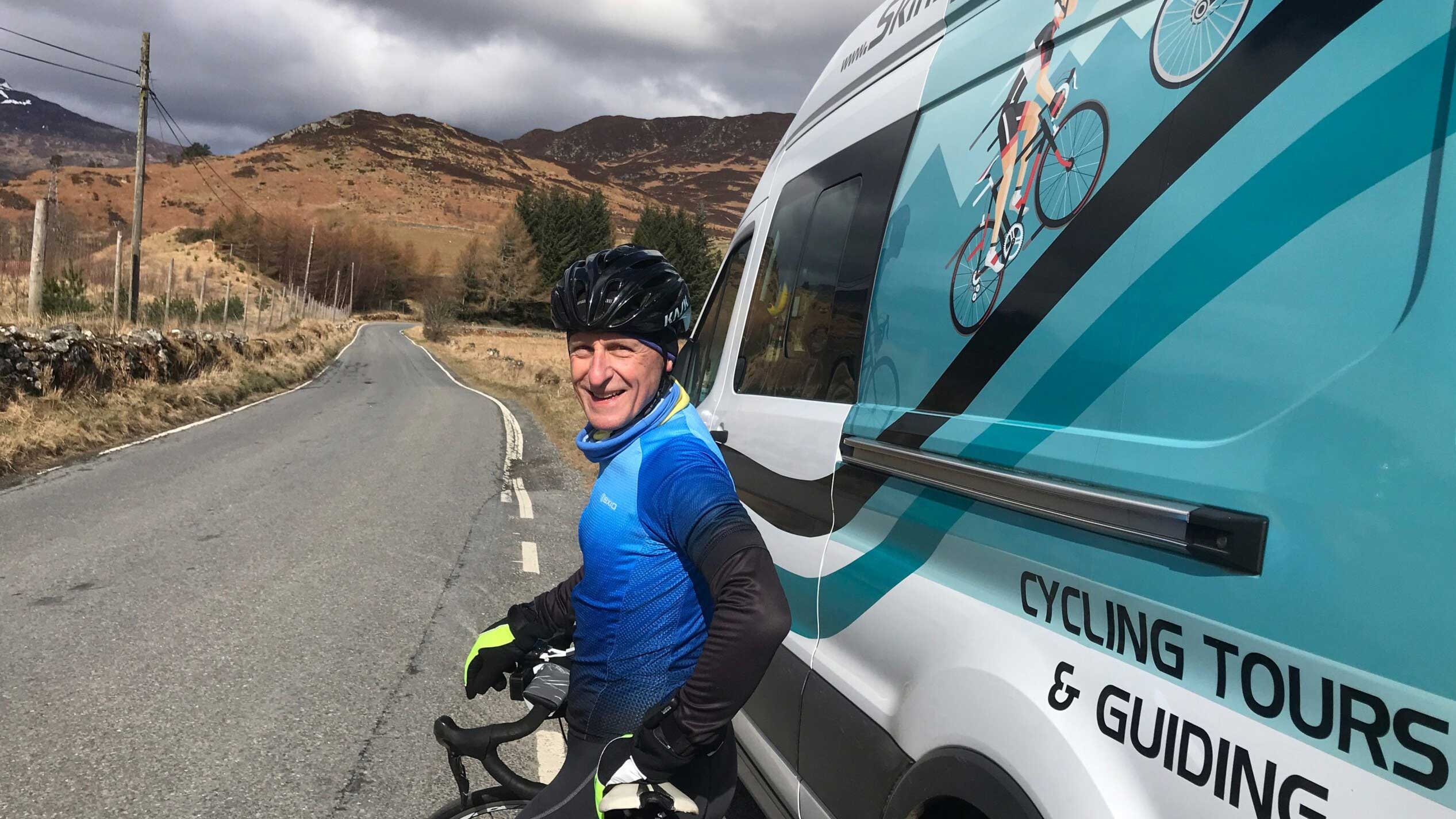A man stands in a Scottish glen beside a Skinny Tyres cycling holiday van
