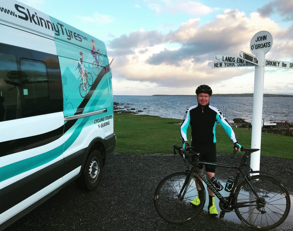 A cyclist stands beside the sign at John O' Groats